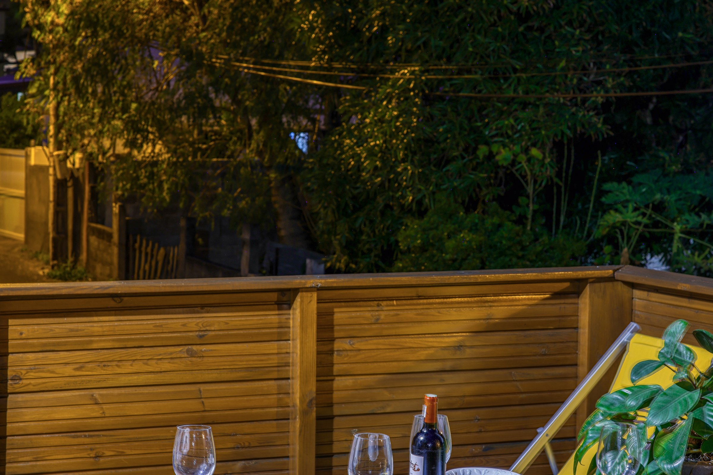 Terrasse du T3 éclairée de nuit, table dressée et végétation au fond