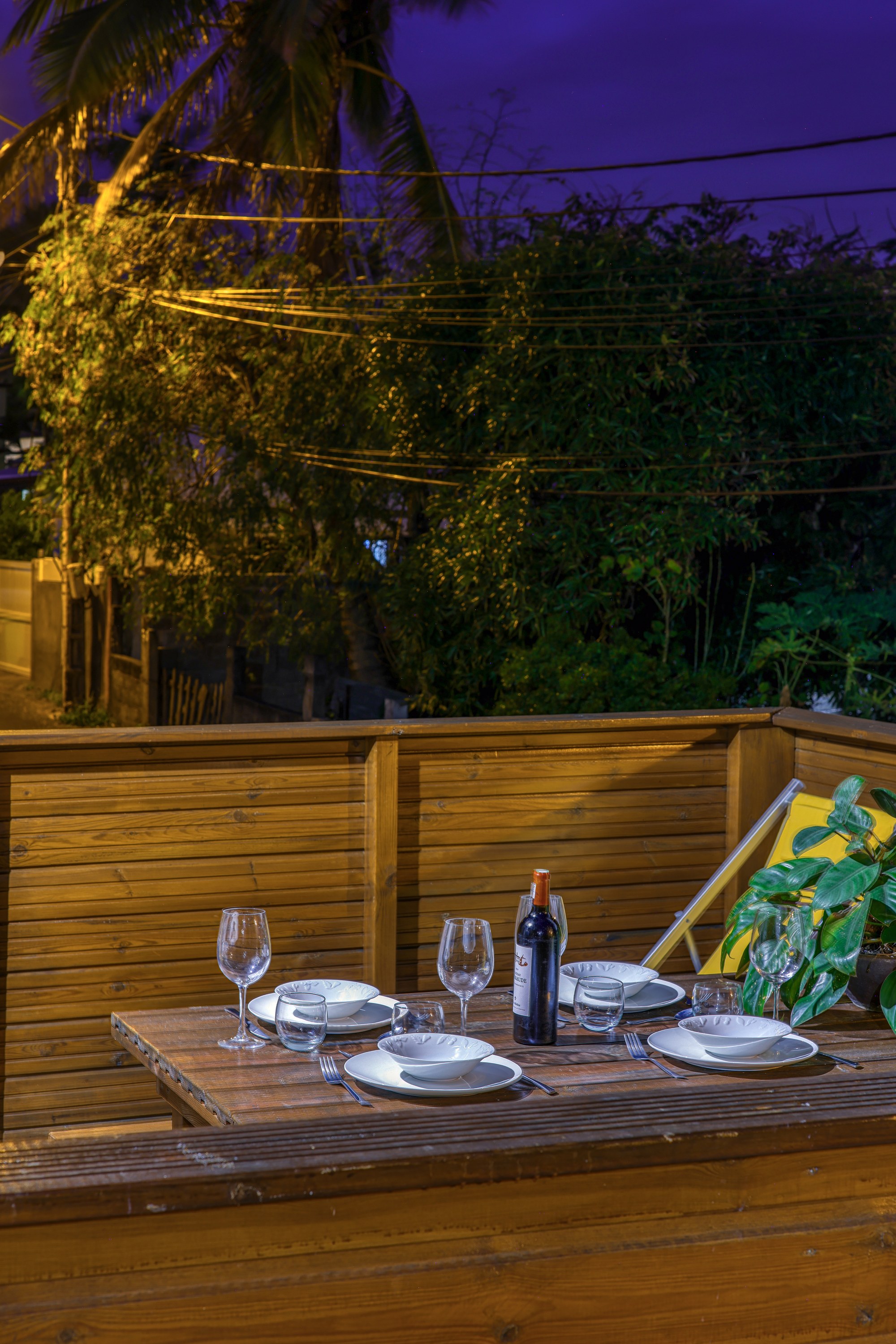 Terrasse du T3 éclairée de nuit, table dressée et végétation au fond
