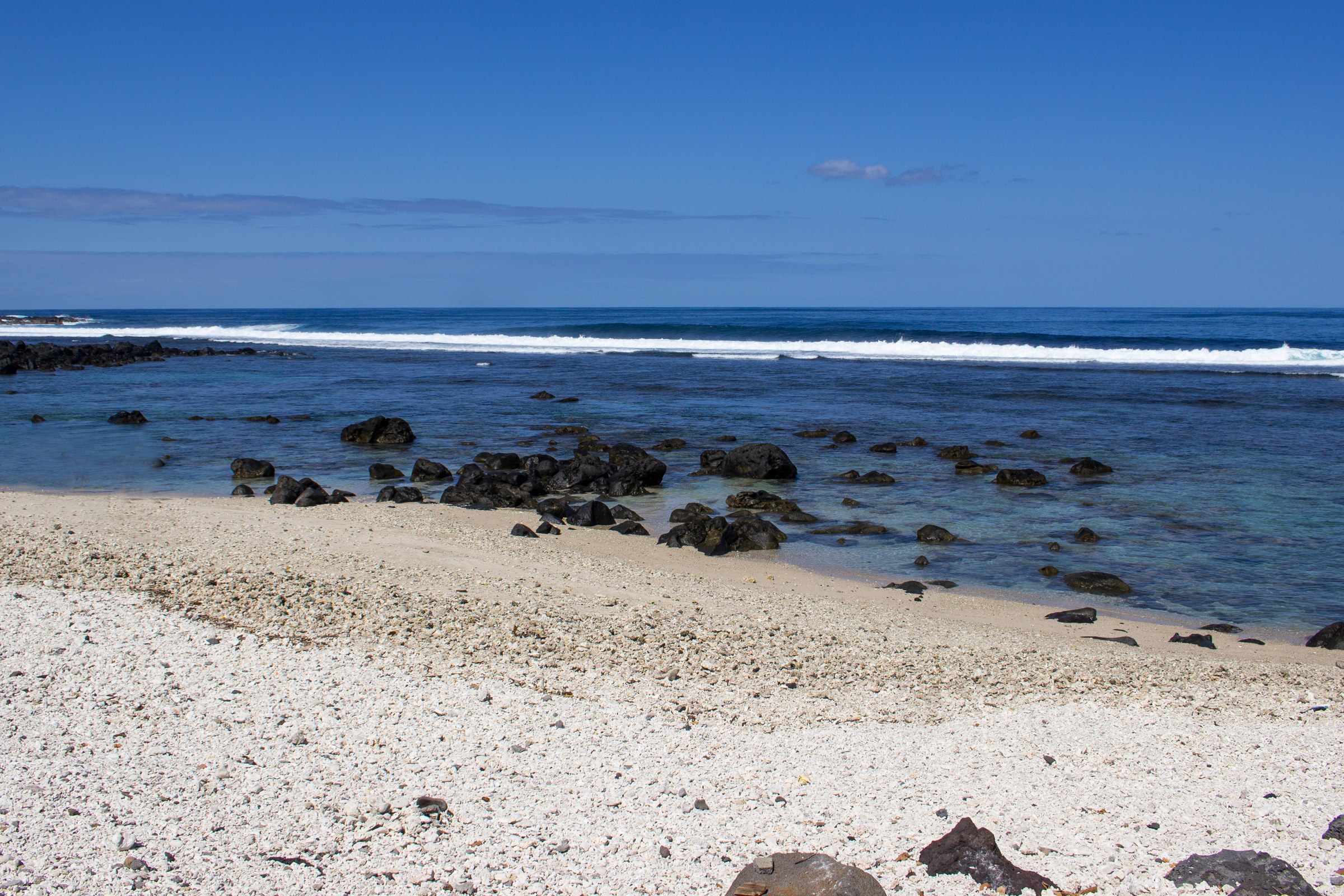 La plage de sable clair et ses rochers volcaniques, face au récif