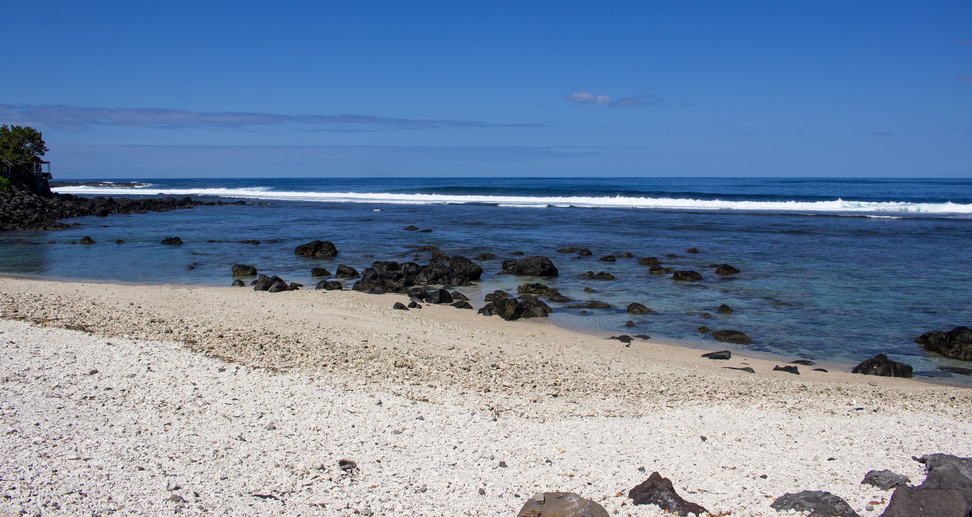 La plage de sable clair et ses rochers volcaniques, face au récif