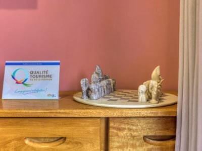 Jeu d’échecs artisanal sur commode en bois sous un mur rose
