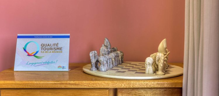 Jeu d’échecs artisanal sur commode en bois sous un mur rose