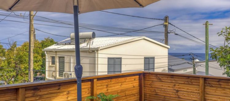 Terrasse en bois équipée d’une table et bancs sous un grand parasol