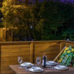 Terrasse éclairée de nuit avec table dressée et végétation en fond